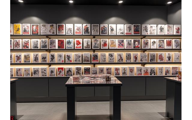 The retail pod within the studio, showcasing a display of limited-edition collectible figures and graphic novels in a well-lit, minimalist setup.